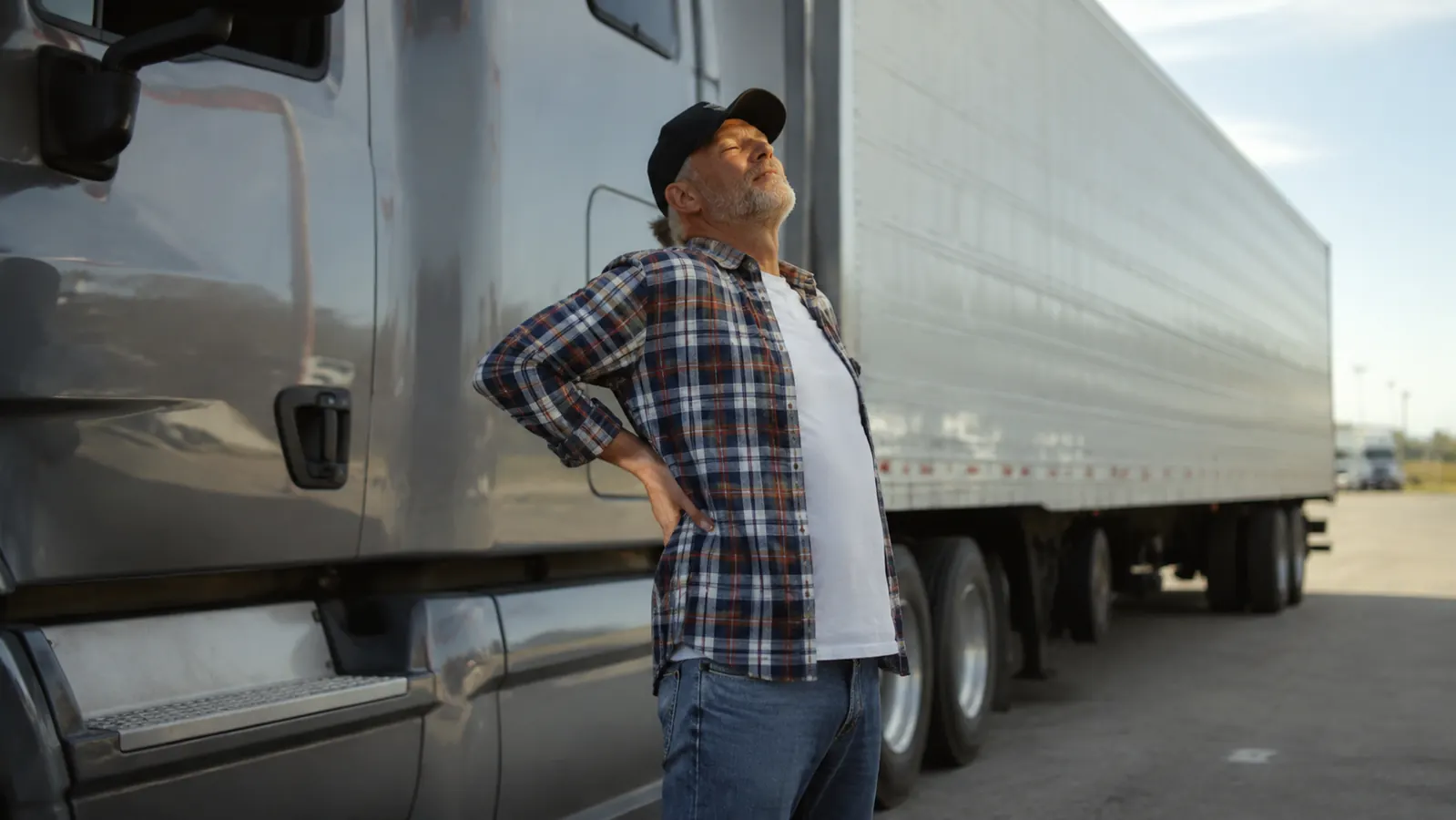 Truck driver stretching beside his rig at a rest stop, relaxed and upright